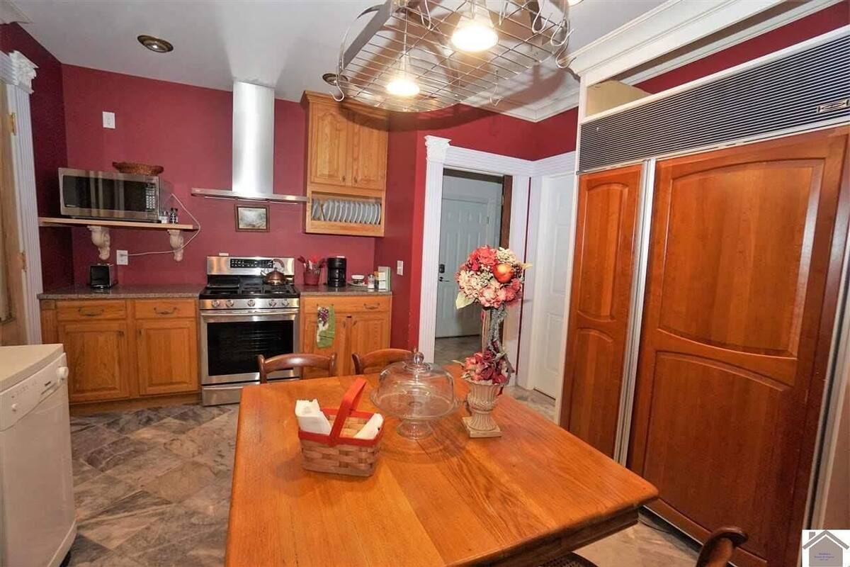 Une cuisine compacte avec des meubles en bois, une cuisinière en acier inoxydable et une table à manger agrémentée d’un vase de fleurs.