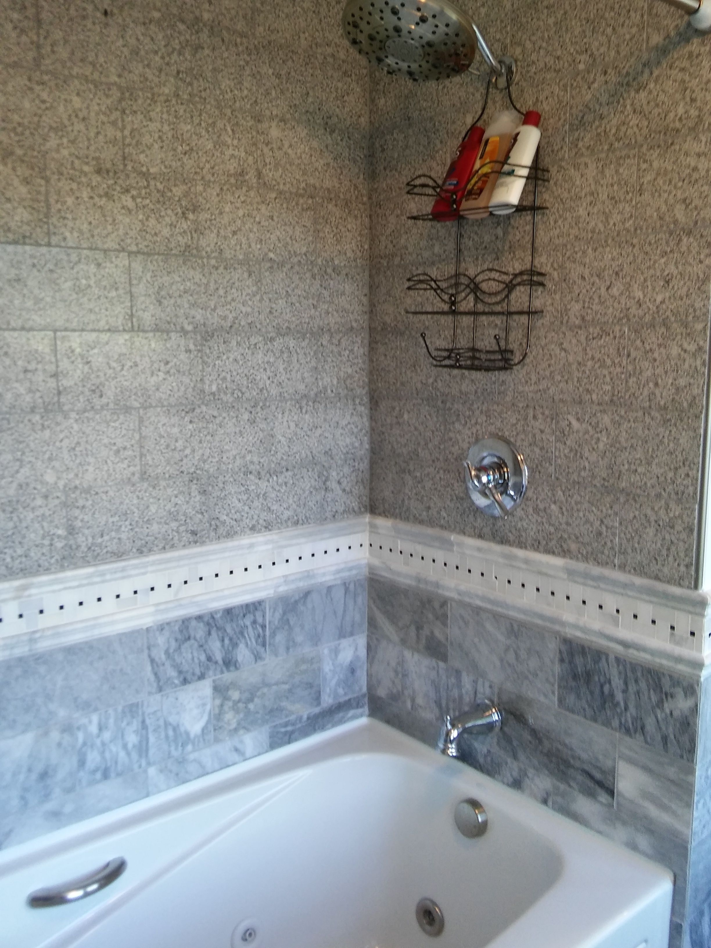 Un baño con una bañera blanca, azulejos de mármol y un perchero con artículos de aseo.