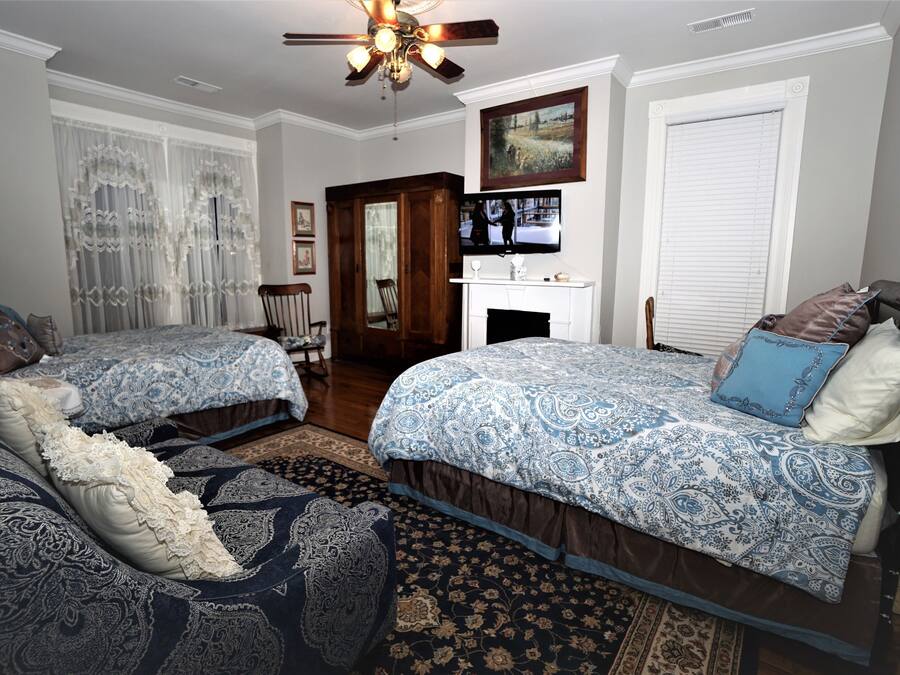 A bedroom with two beds, a ceiling fan, a fireplace, and a television on the wall.