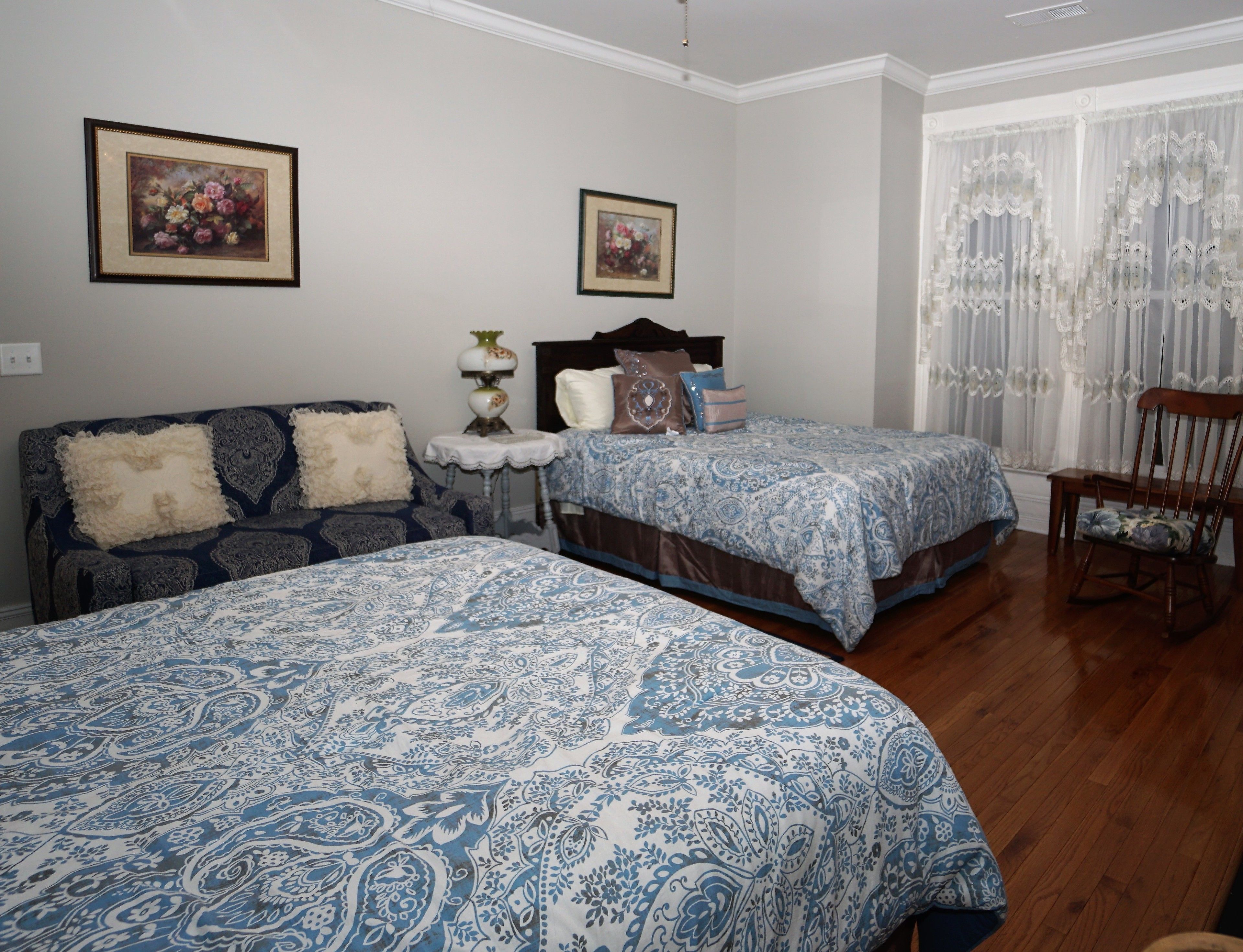 A bedroom with two beds, a wooden floor, and a window with sheer curtains.