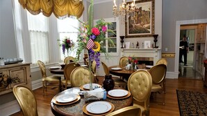 A dining room with a round table set for six, surrounded by upholstered chairs. A vase with flowers and an American flag is on the table. - 1895 Washington Hotel (Paducah)