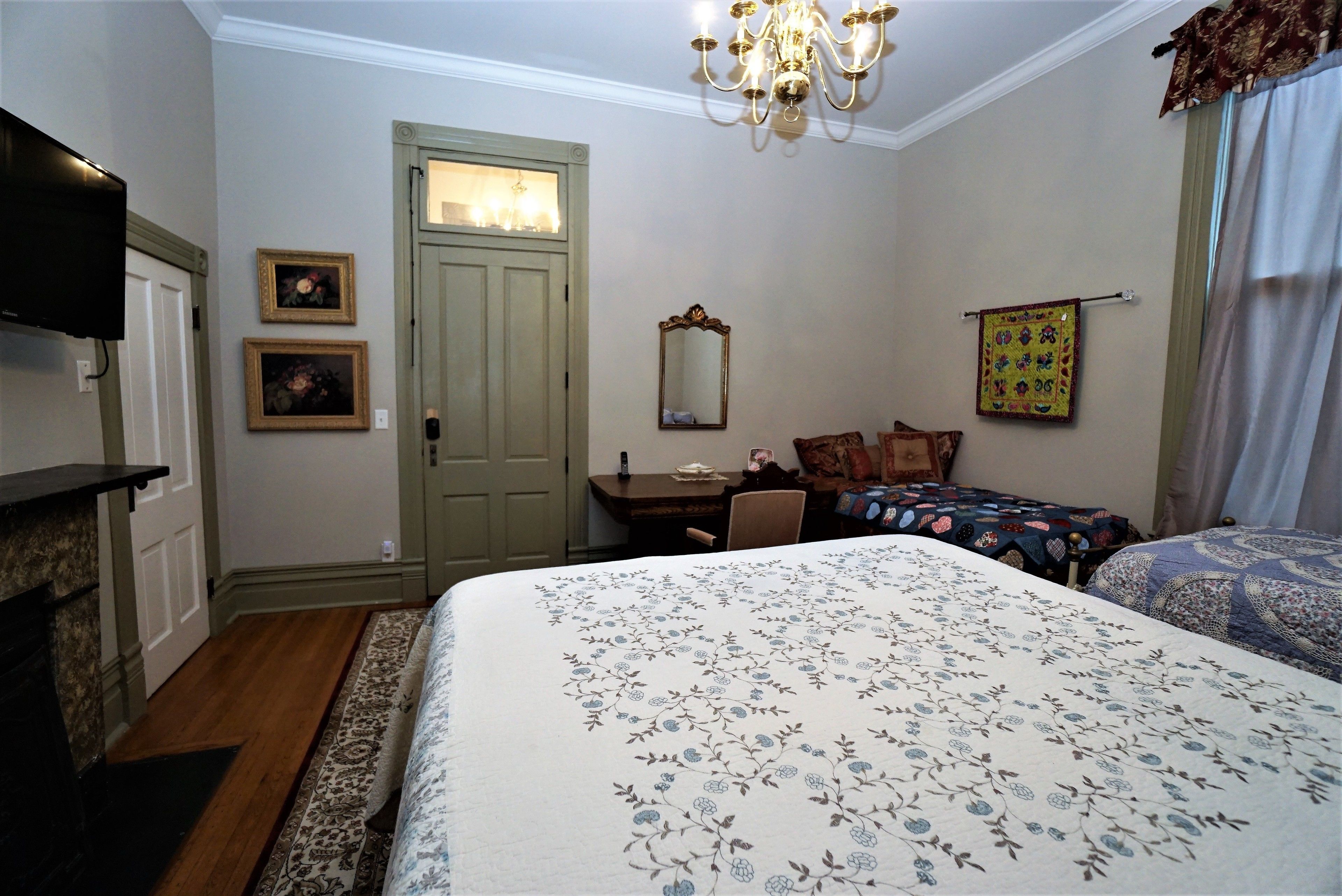 A bedroom with a large bed, a desk, a chair, a television, and a door.