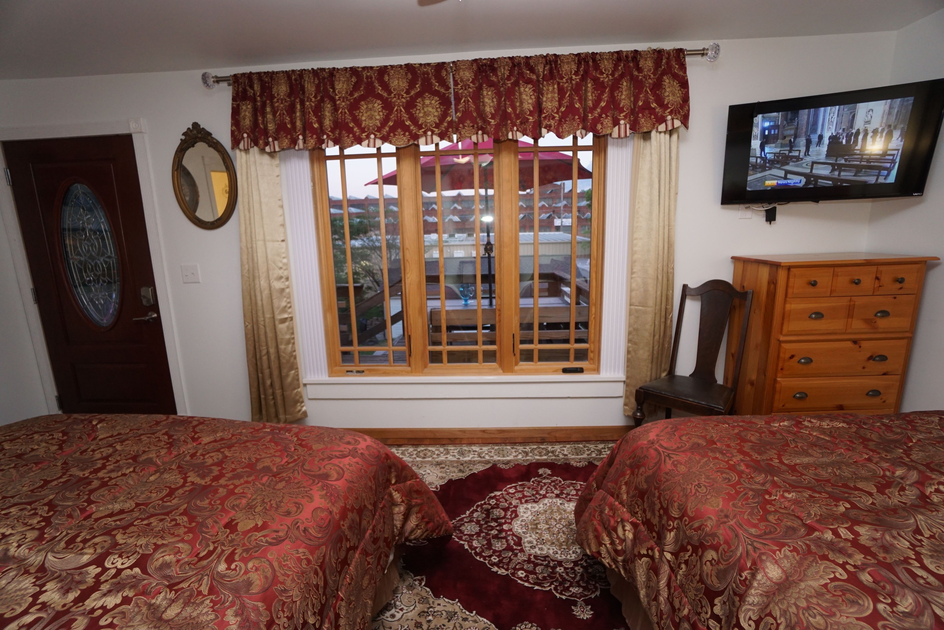 A room with two beds, a wooden dresser, a television, and a window with curtains.
