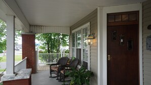 A porch with two wicker chairs, a potted plant, and a wooden door. - 1895 Washington Hotel (Paducah)