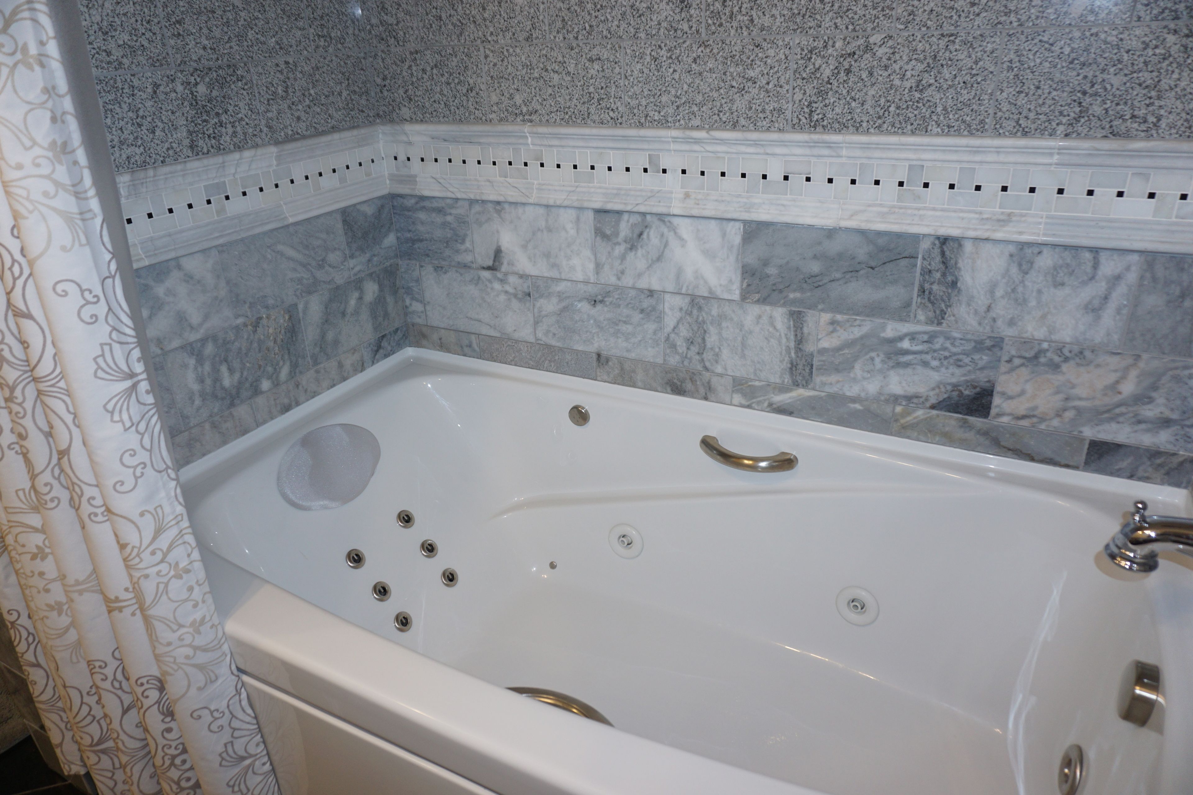 Une baignoire blanche dotée d’un siège intégré, d’un pommeau de douche et d’un panneau de commande.