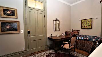 Une pièce comprenant un bureau en bois, une chaise, un lit avec une couverture, un miroir et deux tableaux encadrés accrochés au mur.