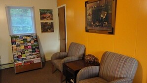 Une pièce avec deux fauteuils à rayures, une petite table, un tableau d’affichage où sont accrochées des cartes postales et un tableau encadré au mur.