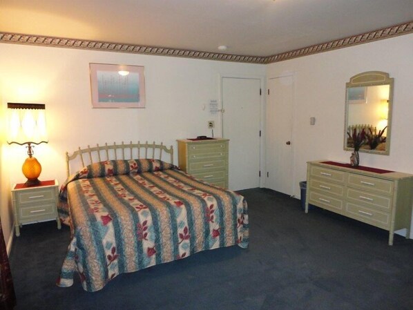 Un dormitorio con cama, cómoda, mesita de noche, lámpara y un cuadro en la pared.