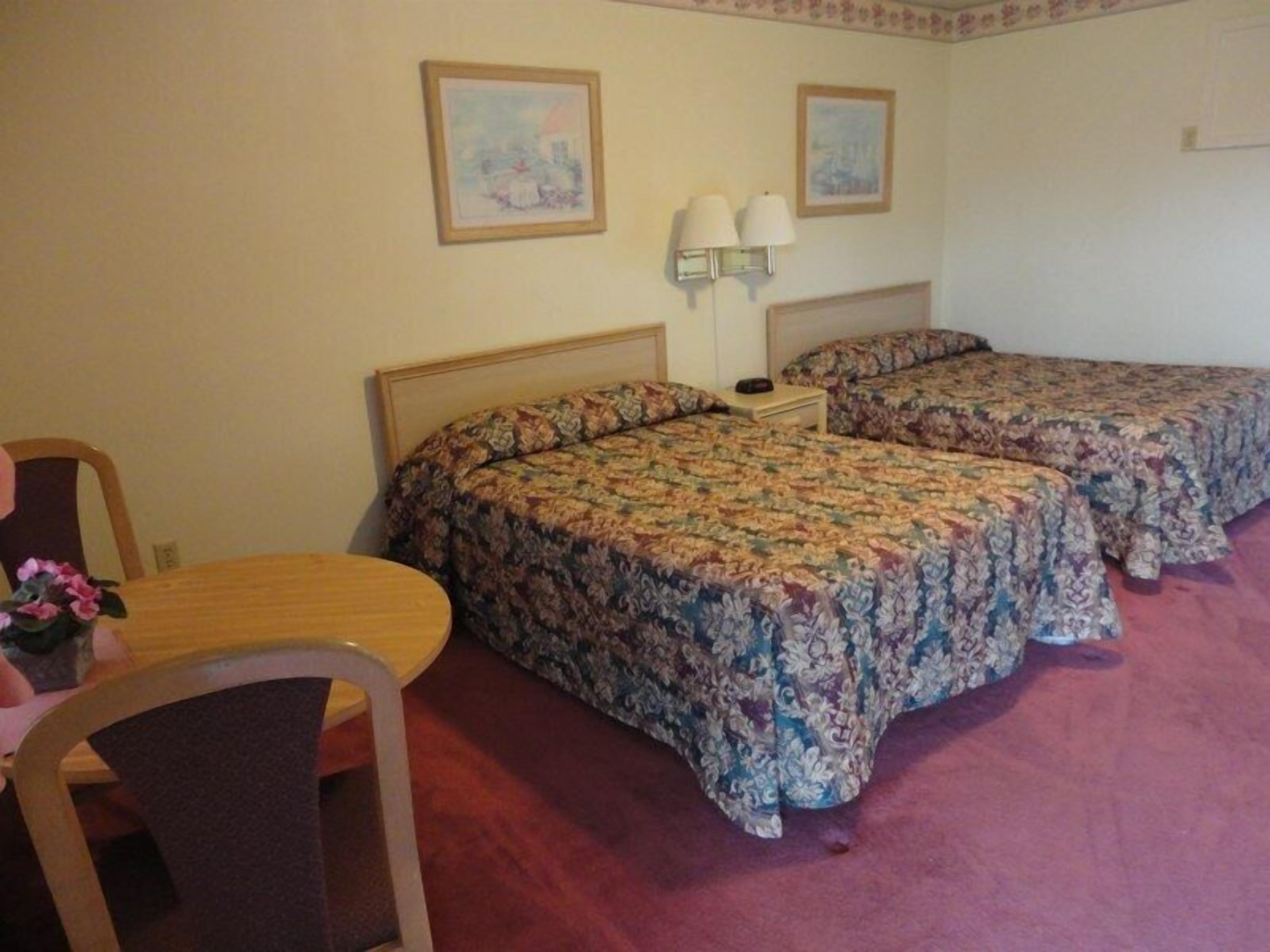A hotel room with two beds, a small table, and two wall-mounted lamps.