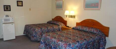 Habitación de hotel con dos camas, un refrigerador pequeño, una lámpara y una silla.