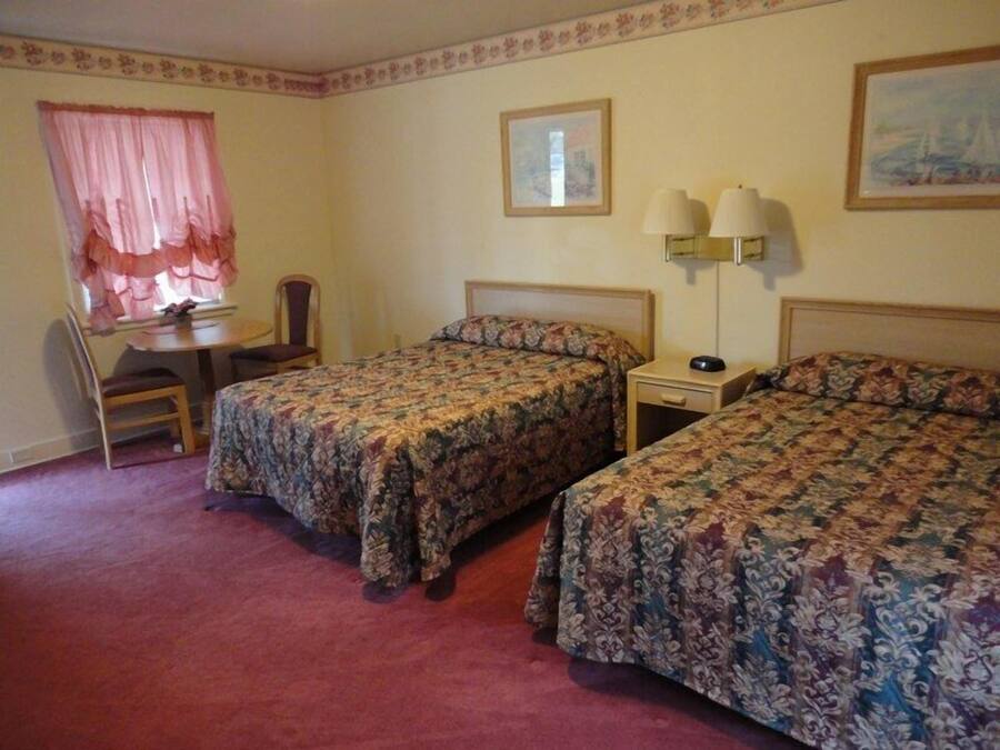 A hotel room with two single beds, a desk with a chair, a small table, and two wall lamps.