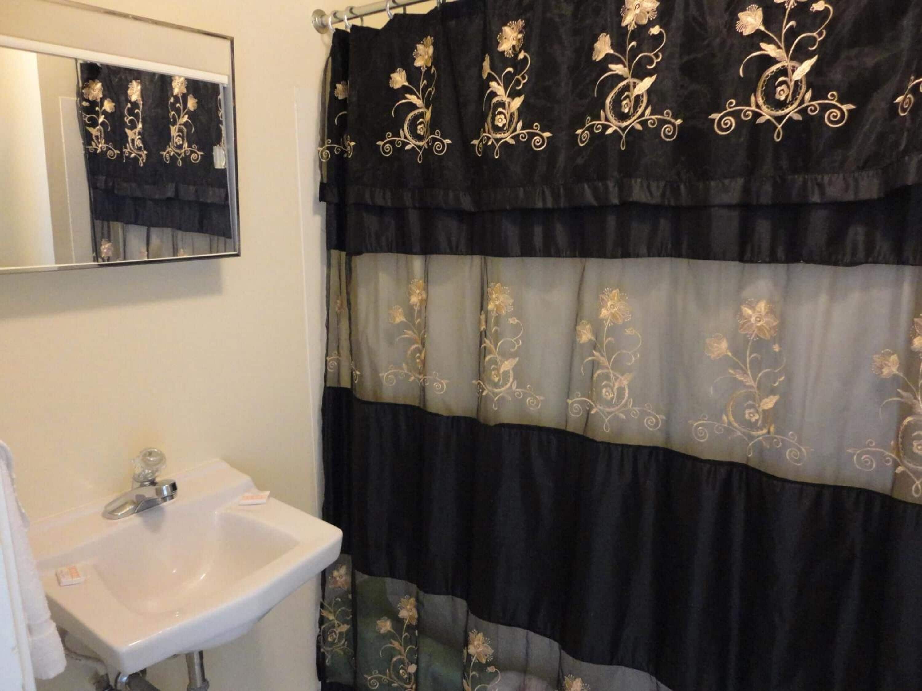 A bathroom with a white sink, a mirror, and a black and gold shower curtain.