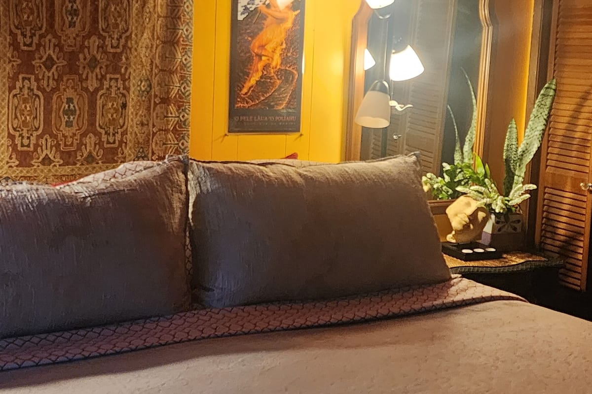 Una cama con un cabecero estampado, un cartel en la pared, un espejo y una planta en maceta.