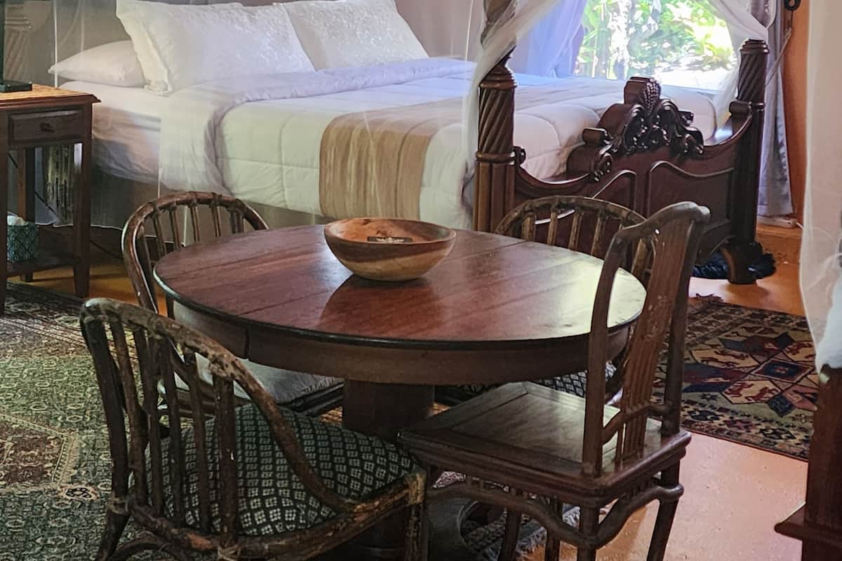 Una cama con dosel y cuatro columnas, una mesa de comedor de madera con sillas y una alfombra estampada.