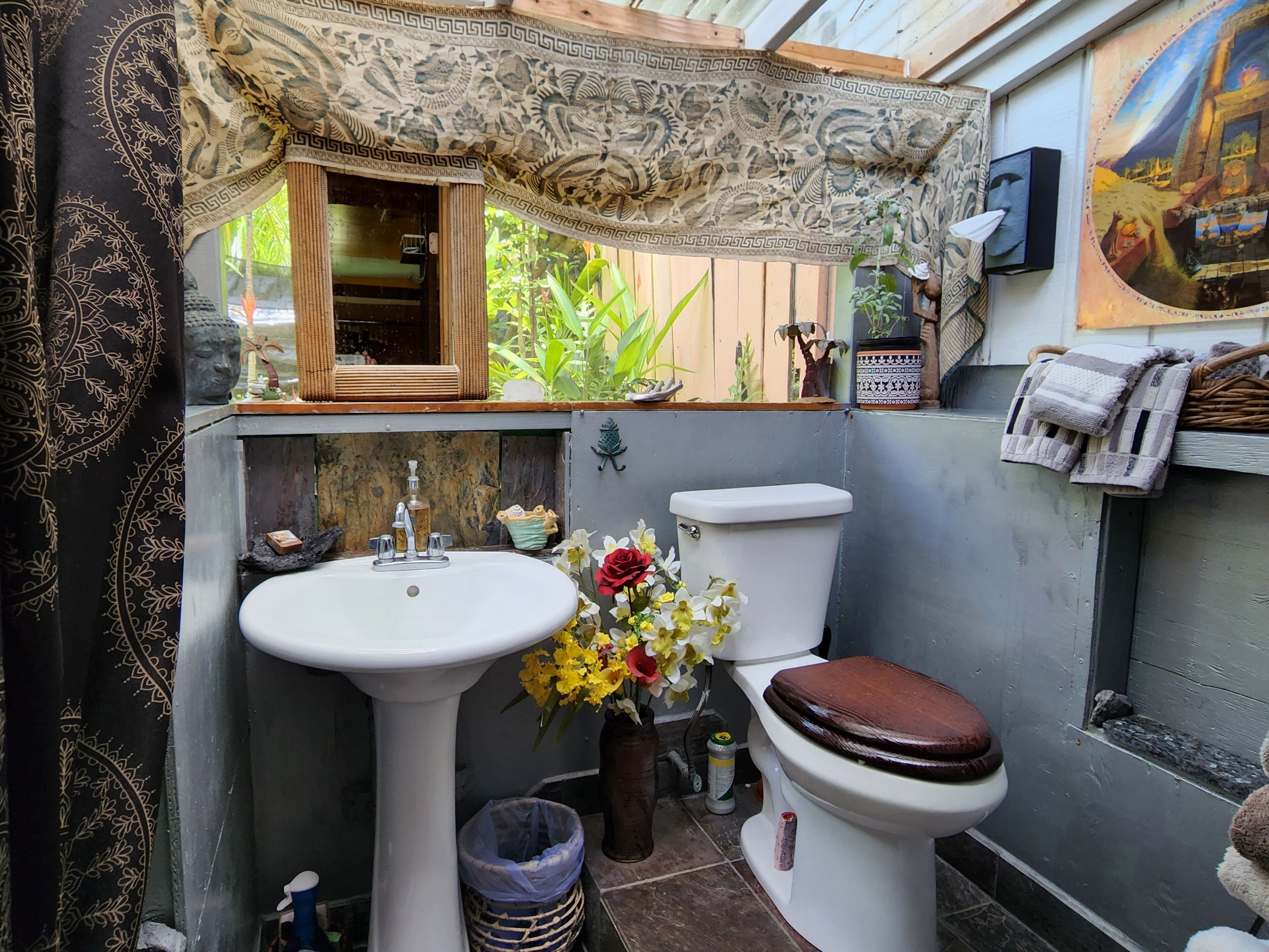 A compact bathroom with a pedestal sink, toilet, and a window with a view of greenery.