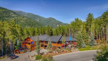 A lodge with a wooden exterior, multiple decks, and a view of surrounding forest and mountains.