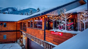 A cabin restaurant with a wooden exterior, a sign indicating its name, and a view of snow-covered mountains in the background. - Earl Grey Lodge (Panorama)