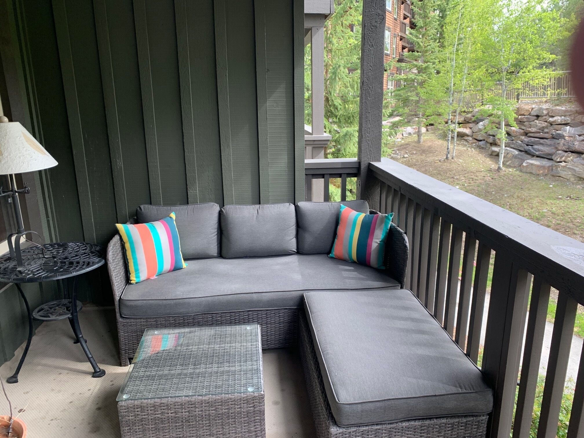 A covered outdoor seating area with a curved sofa and a small table, surrounded by a wooden railing.