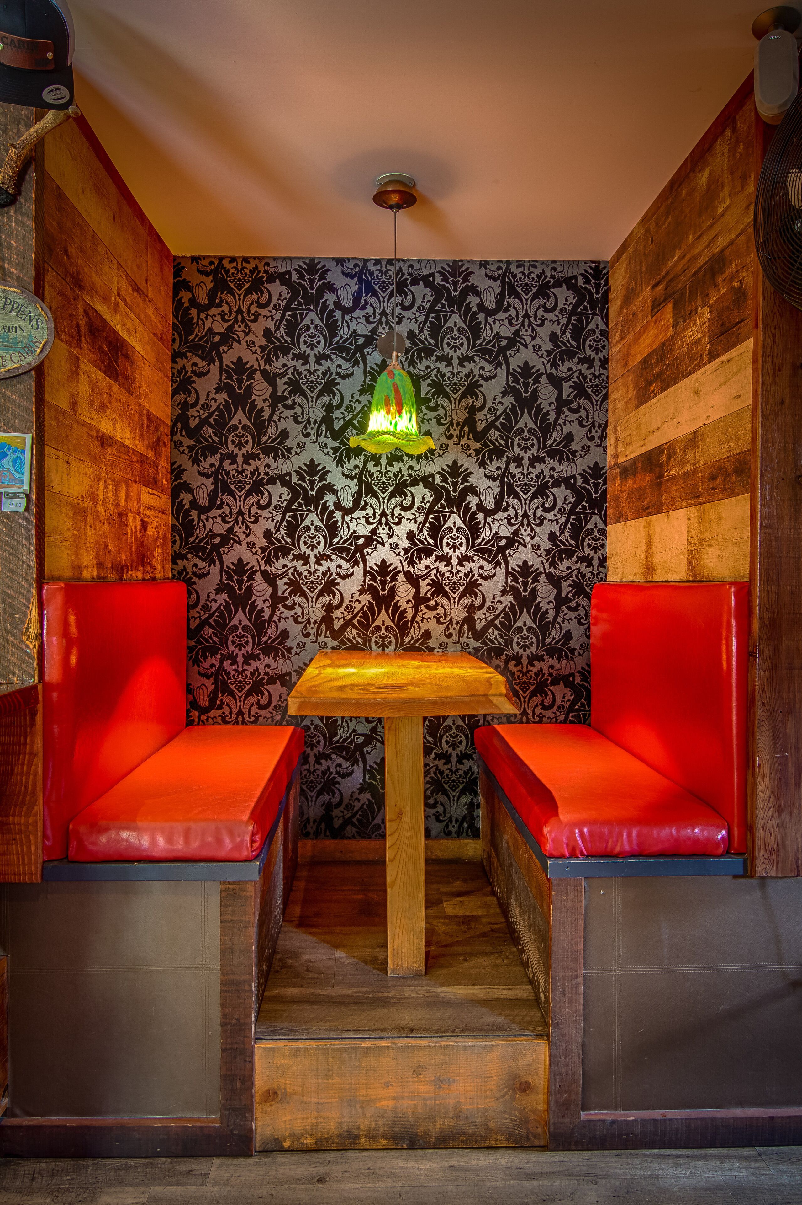 A corner seating area with a wooden table and red cushioned benches, a patterned wallpaper, and a hanging light fixture.
