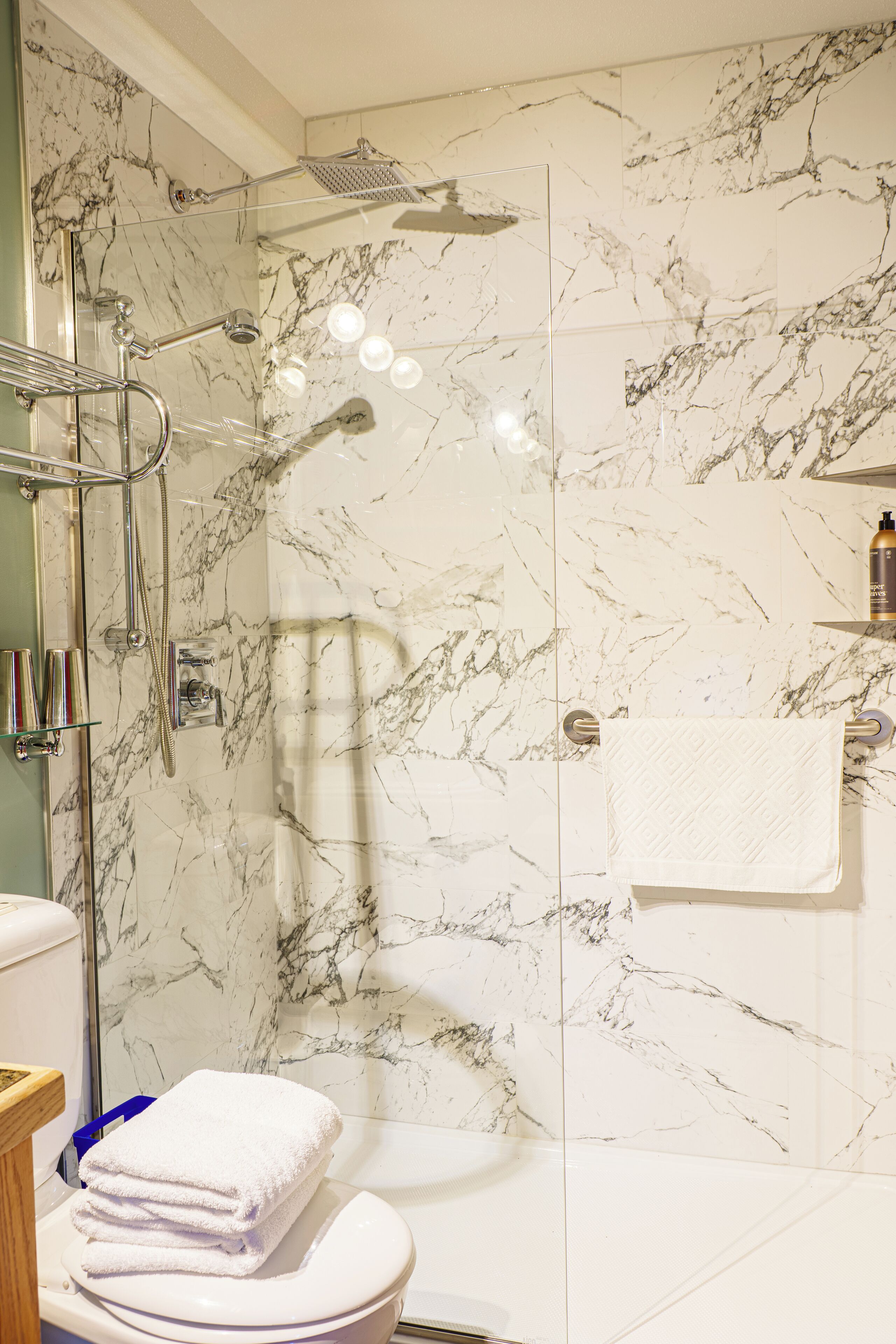 A bathroom with a glass-enclosed shower, marble walls, a toilet, and a towel rack.