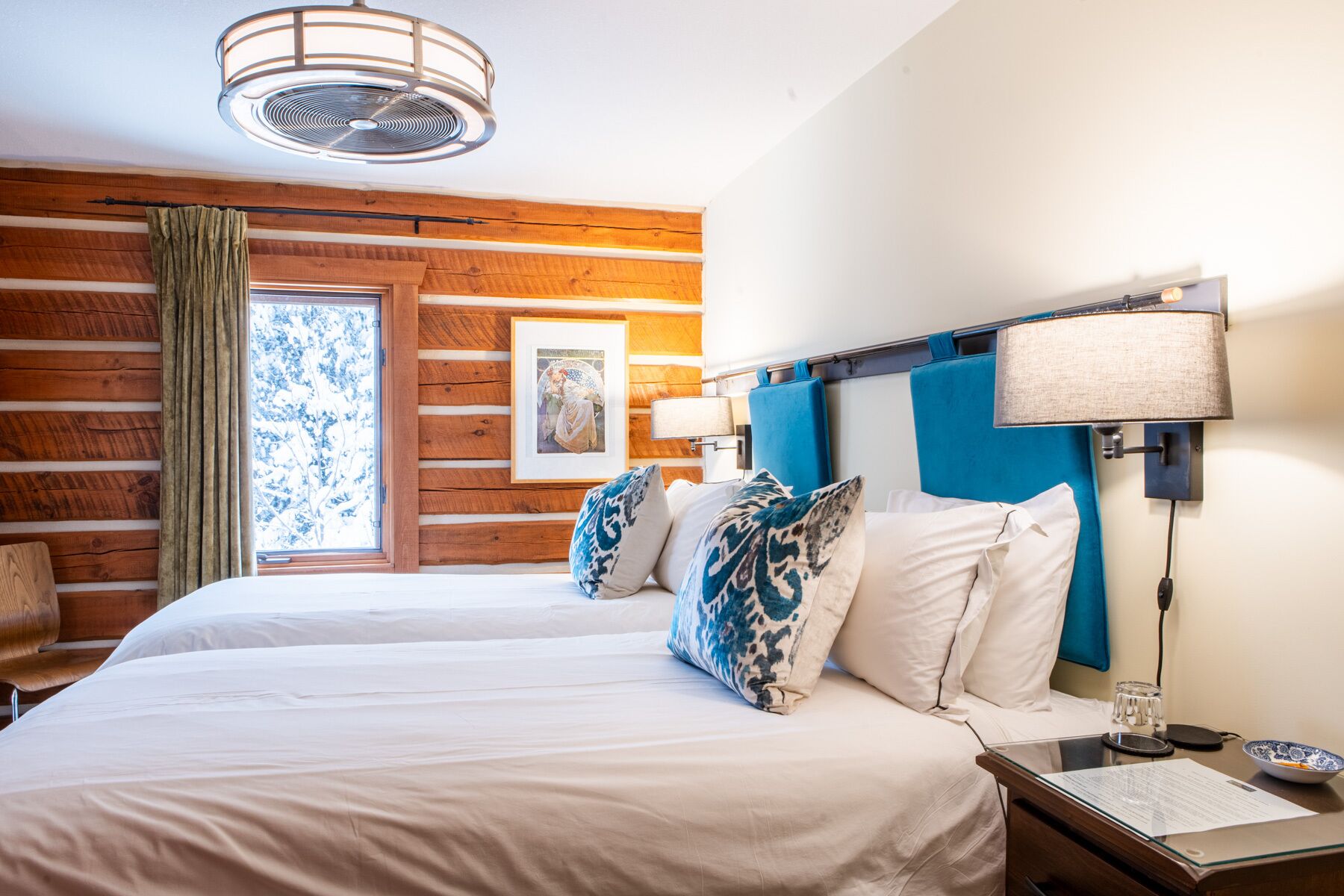 A hotel room with a wooden wall, a bed with white and blue patterned pillows, a nightstand with a lamp, and a framed picture on the wall.
