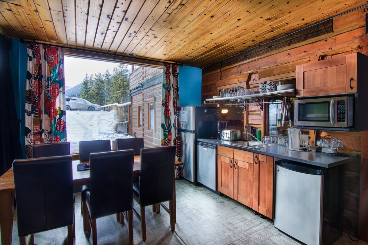 A cozy cabin-style kitchen with wooden cabinets, a stainless steel refrigerator, a microwave, and a dining area with a table and chairs.