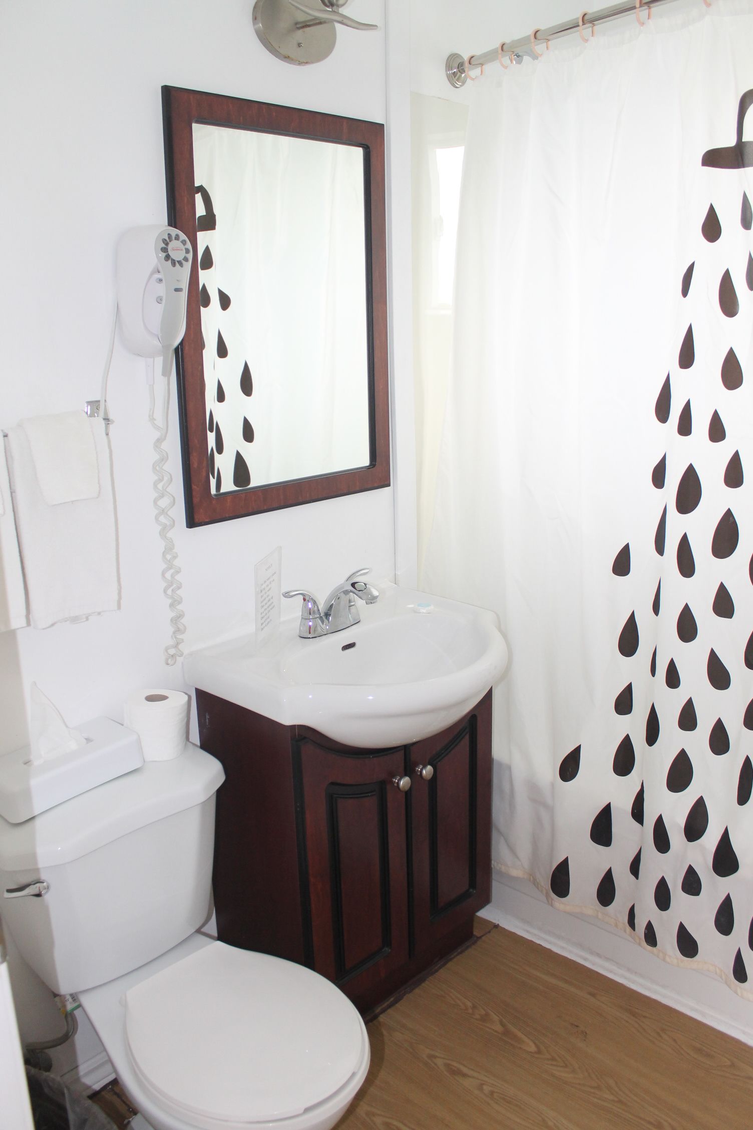 Un baño con inodoro blanco, lavamanos, espejo y cortina de ducha con diseño de hojas.