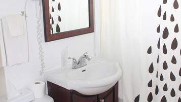 Un baño con inodoro blanco, lavamanos, espejo y cortina de ducha con diseño de hojas.