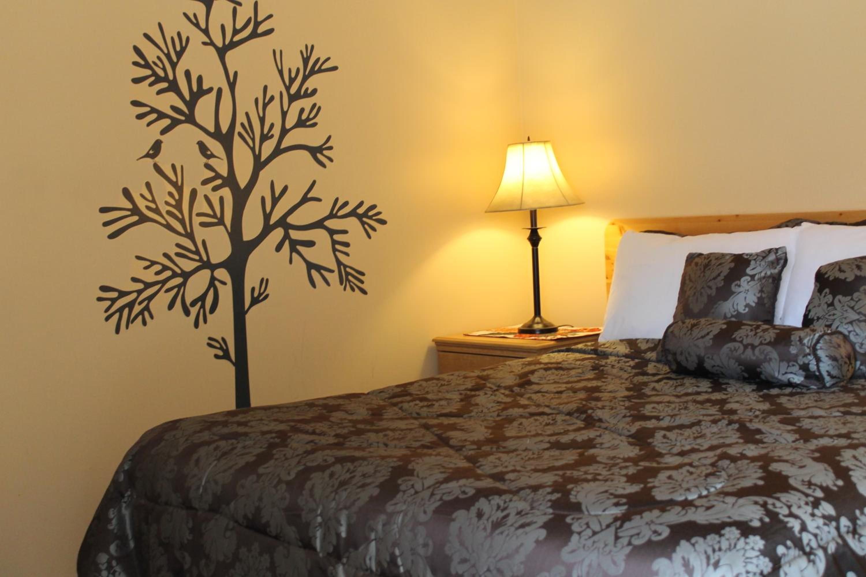 A hotel room with a bed, a nightstand, a lamp, and a wall decoration of a tree.