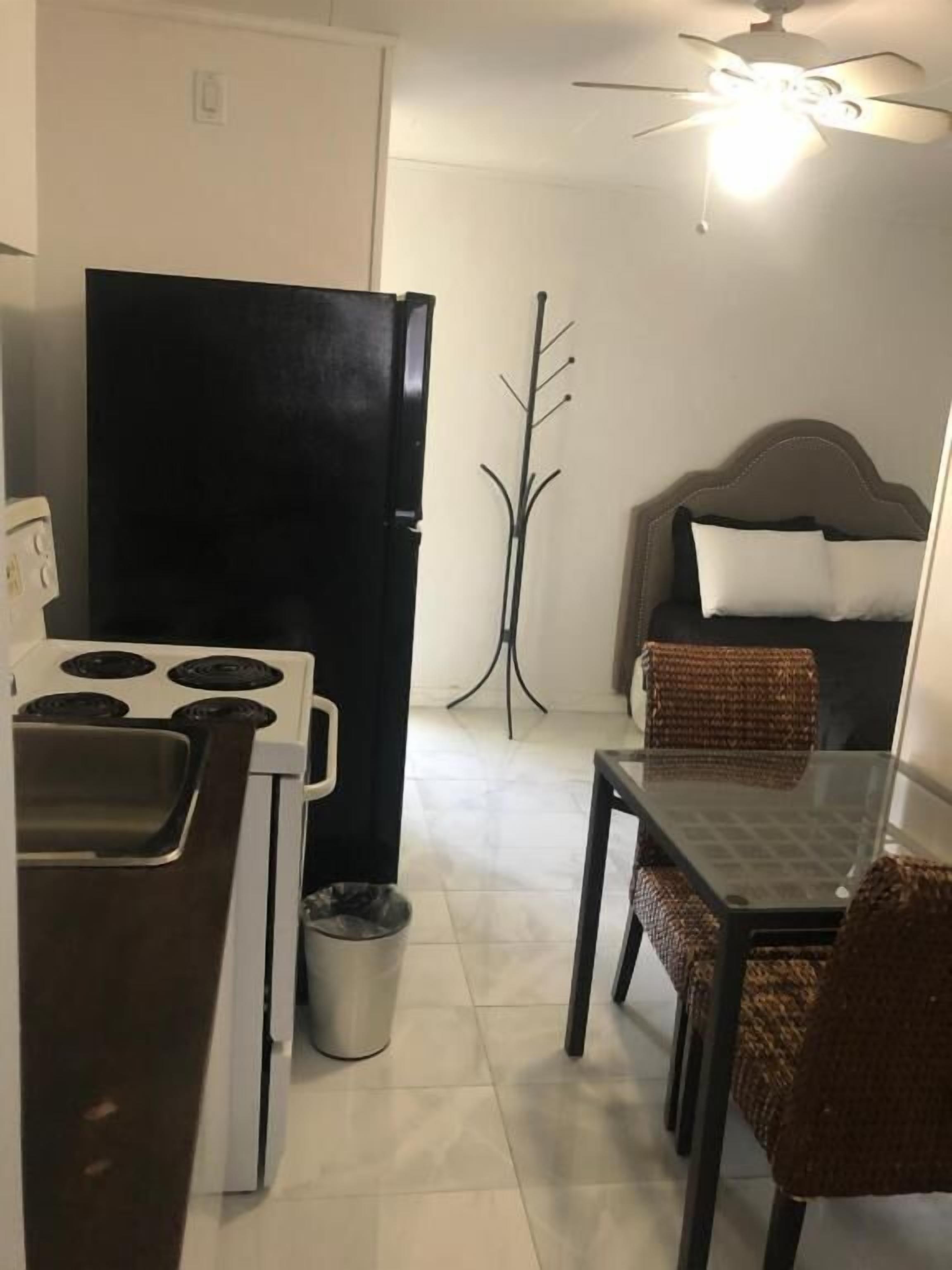 Une cuisine compacte équipée d’un réfrigérateur, d’une cuisinière et d’un évier. On y trouve une table à manger avec des chaises et un ventilateur de plafond.
