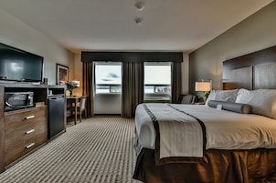 Quarto de hotel com cama, televisão, escrivaninha com abajur e vista para o exterior.
