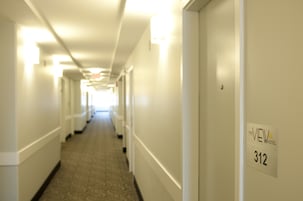 Um corredor de hotel com chão coberto de carpete, paredes brancas e uma placa indicando o quarto 312.