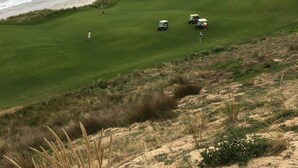 A golf course with a lighthouse in the distance, sandy dunes, and a beach.