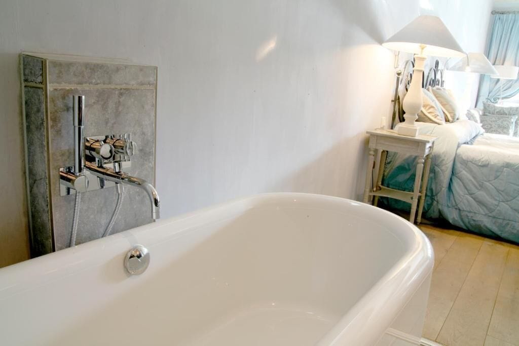 Un baño moderno con una bañera independiente, zona de ducha y una mesita de noche con lámpara.