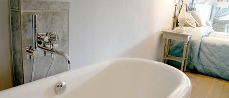 Un baño moderno con una bañera independiente, zona de ducha y una mesita de noche con lámpara.