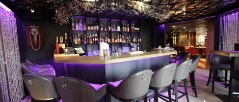 Zona de bar con mostrador, varios taburetes y estantes llenos de botellas.