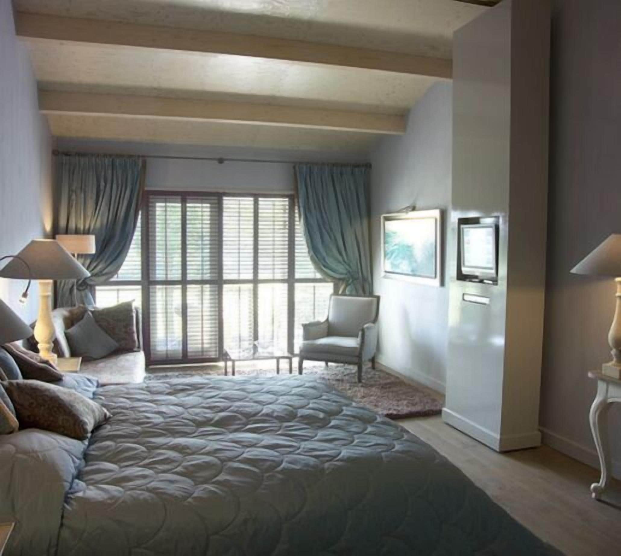 Ein Schlafzimmer mit einem großen Bett, einem Sessel, einem Schreibtisch und einem Fenster mit Vorhängen.