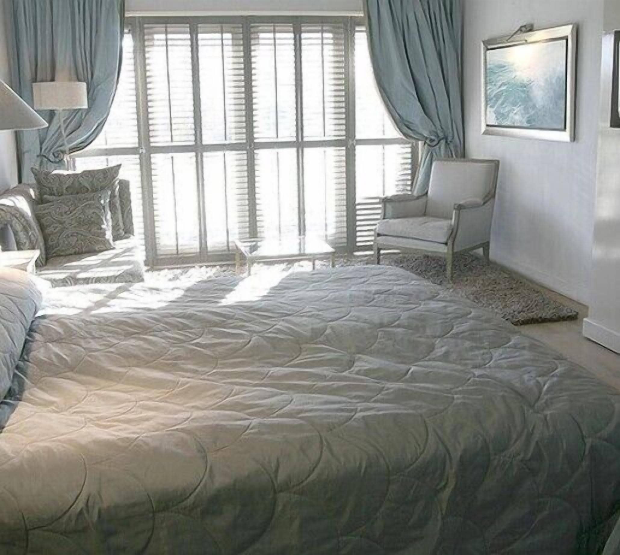 A bedroom with a large bed, a chair, and a window with blinds.