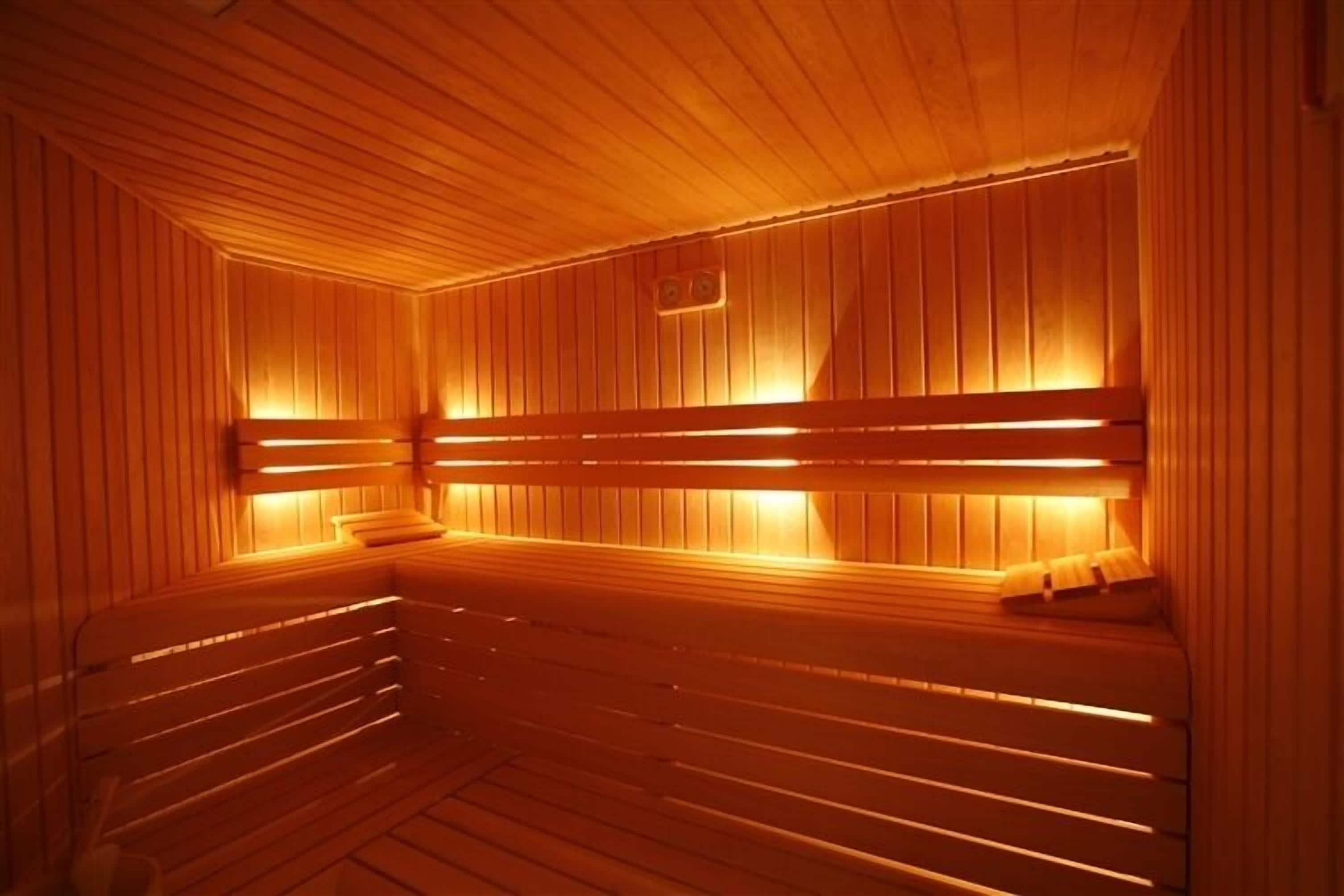 A sauna with wooden benches and slatted walls, illuminated by warm lighting.
