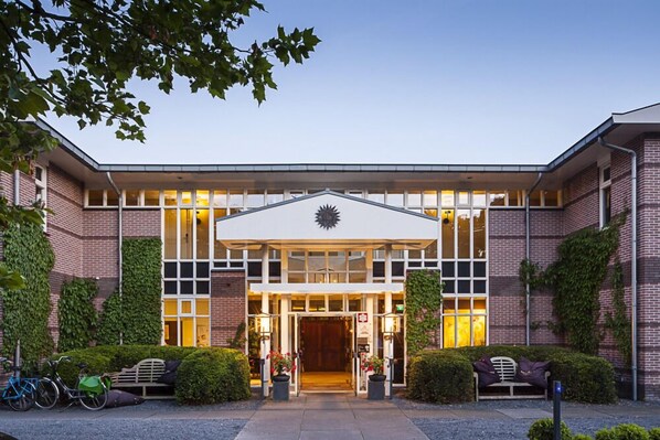A modern building with a symmetrical facade, large windows, and a central entrance with a sun-like design.