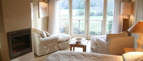 A room with a fireplace, two sofas, a bed, and a view of the outdoors through large windows.