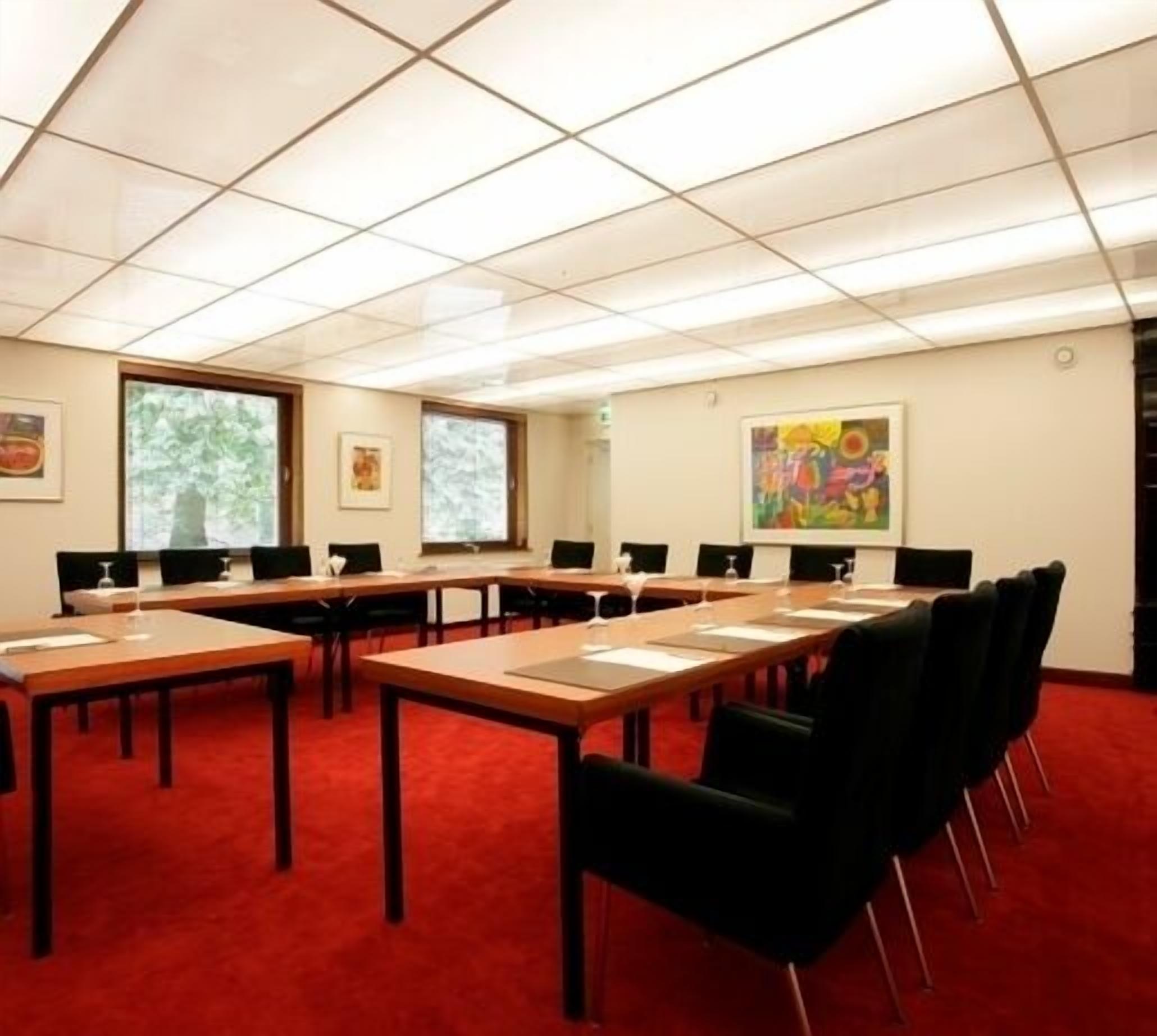Ein Konferenzraum mit mehreren Tischen und Stühlen, großen Fenstern und Kunstwerken an den Wänden.