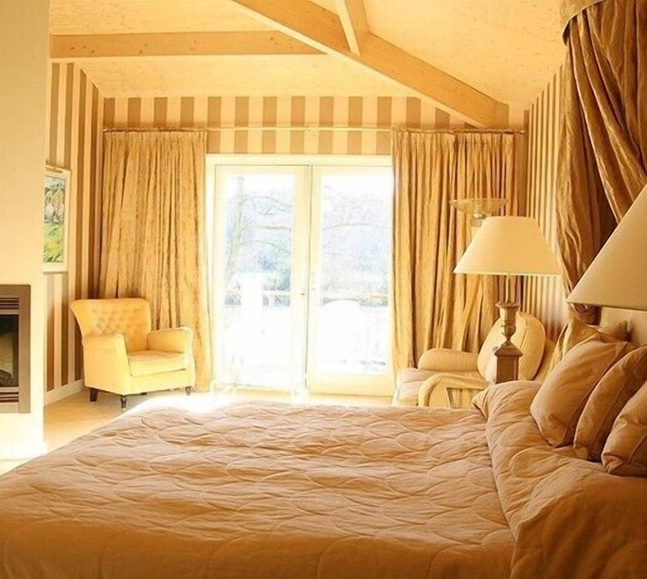 Ruime slaapkamer met een groot bed, een stoel, een lamp en uitzicht op de natuur via een schuifdeur.