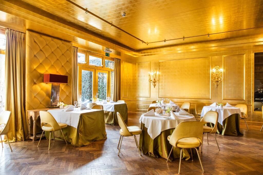 Ein Essbereich mit runden Tischen und Stühlen, Holzboden und einer warmen, goldenen Einrichtung.