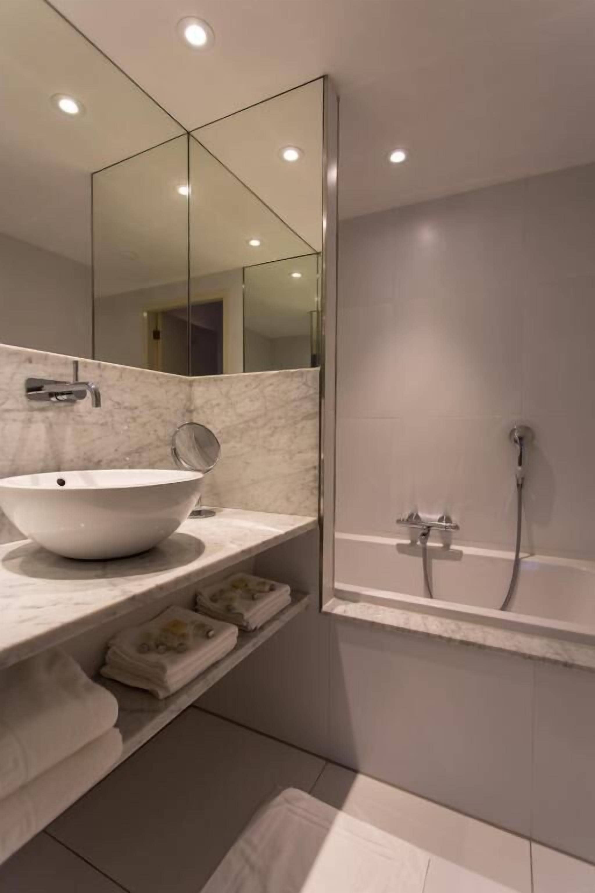 Un baño moderno con un espejo grande, un lavabo blanco y una bañera.