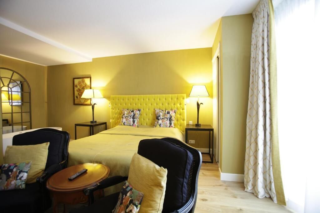 A hotel room with a large bed, two bedside tables with lamps, a chair, a small table with a remote control, and a window with curtains.