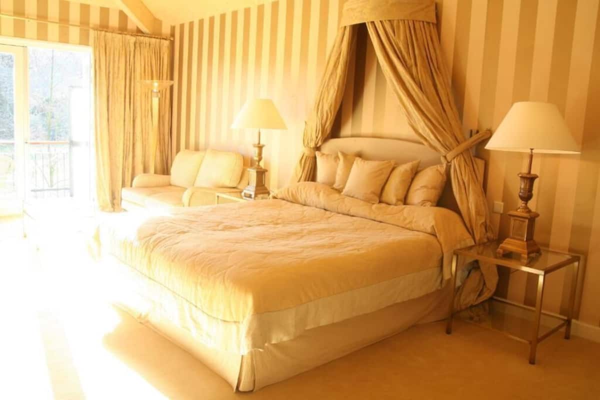 A large bed with a canopy, two bedside tables with lamps, a sofa, and a view of the outdoors.