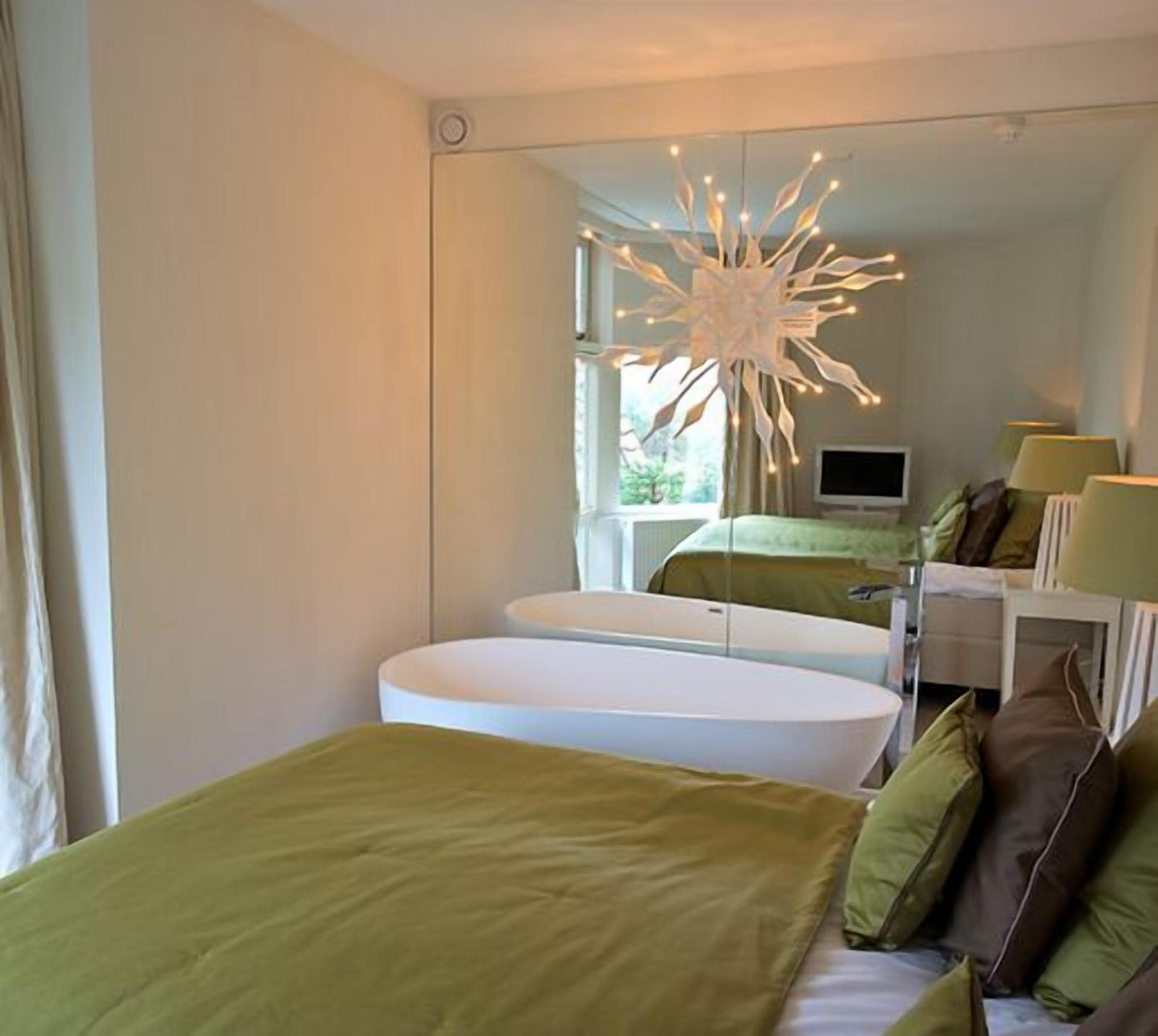Een moderne slaapkamer met een groot bed, een witte badkuip en een bijzondere plafondlamp.