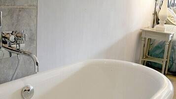 Un baño con una bañera blanca, una mesita con una lámpara y un revestimiento de azulejos.