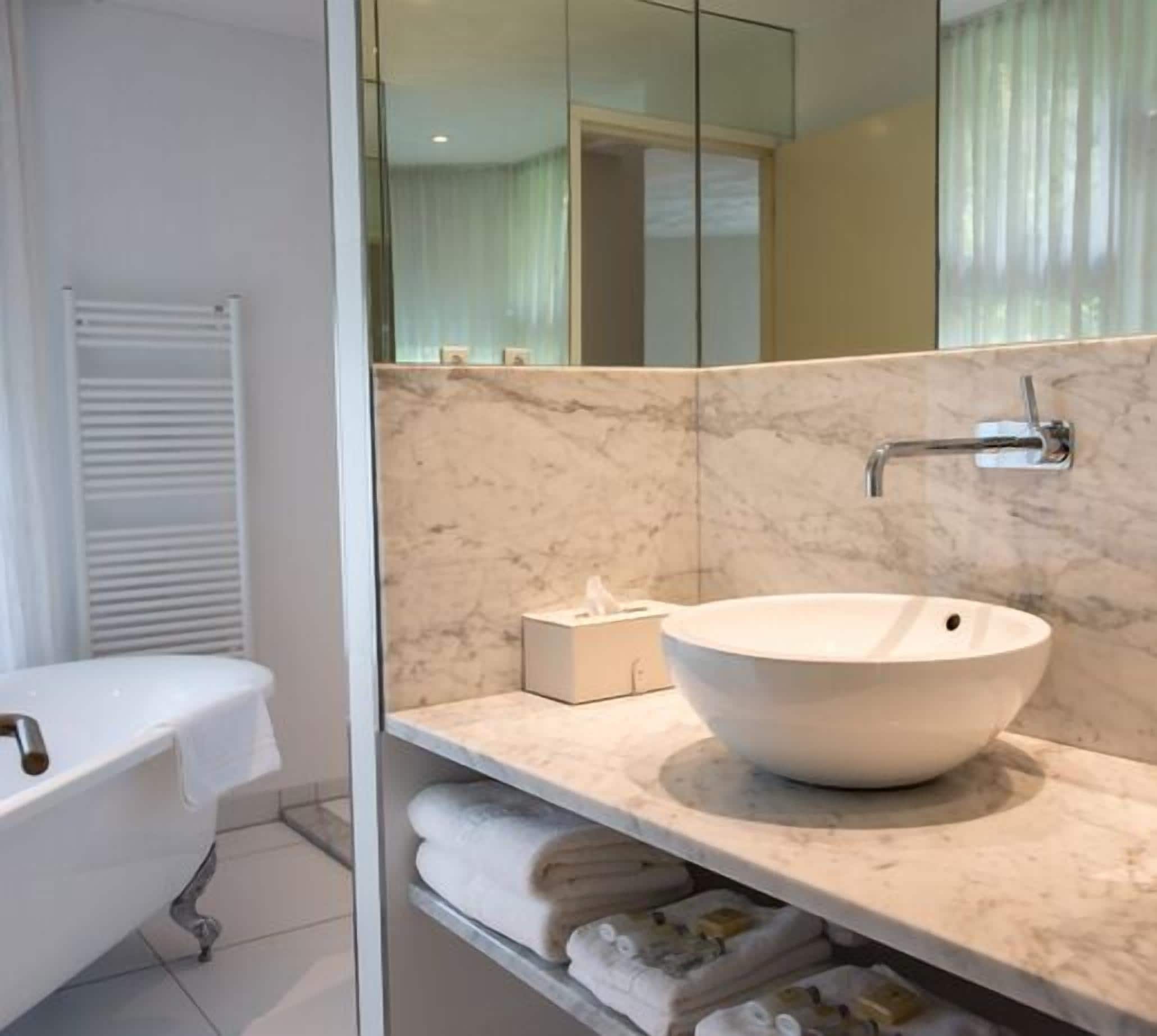 A modern bathroom with a freestanding bathtub, a large mirror, and a marble countertop with a vessel sink.